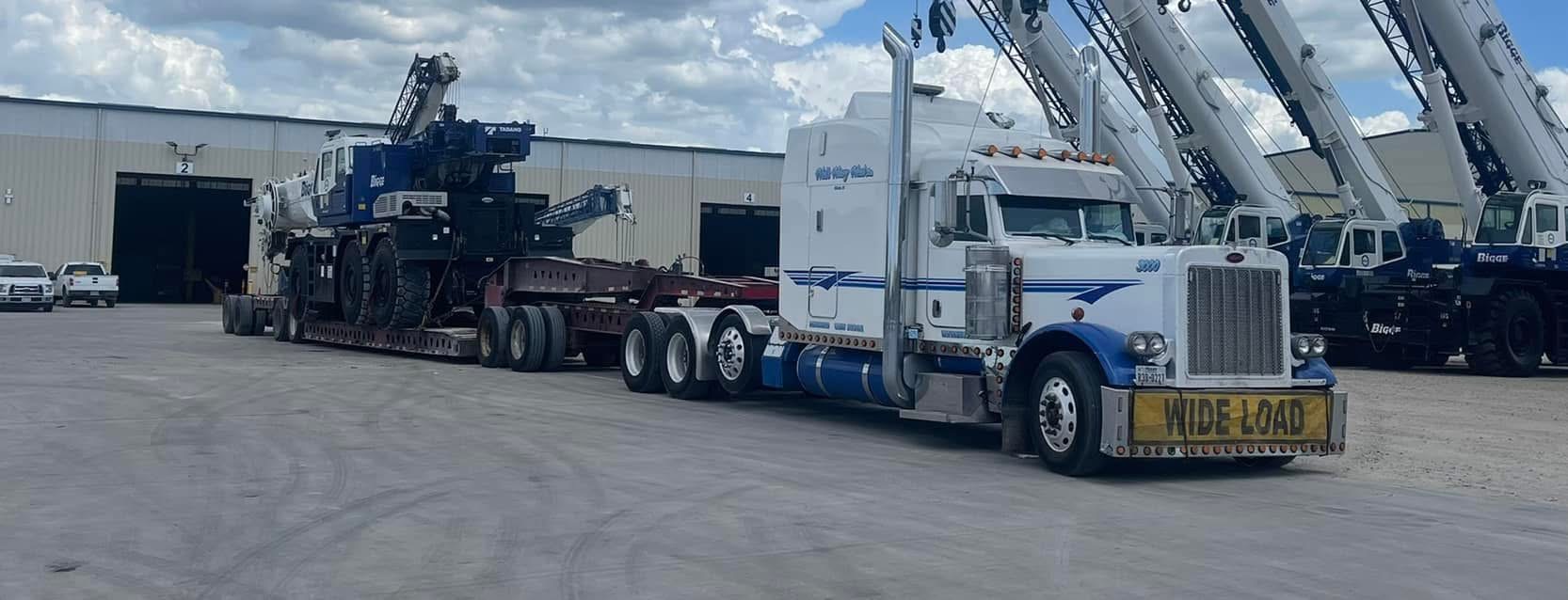 White and blue Peterbilt with WIDE LOAD banner hauling a Tadano Bigge crane