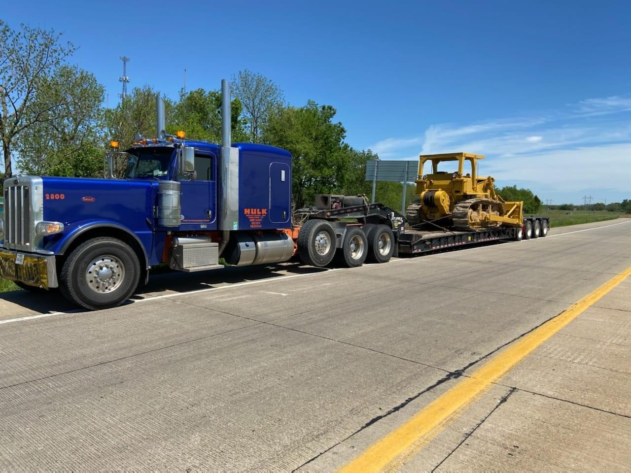 Blue Peterbilt lowboy hauling a vintage Caterpillar dozer on a Texas highway