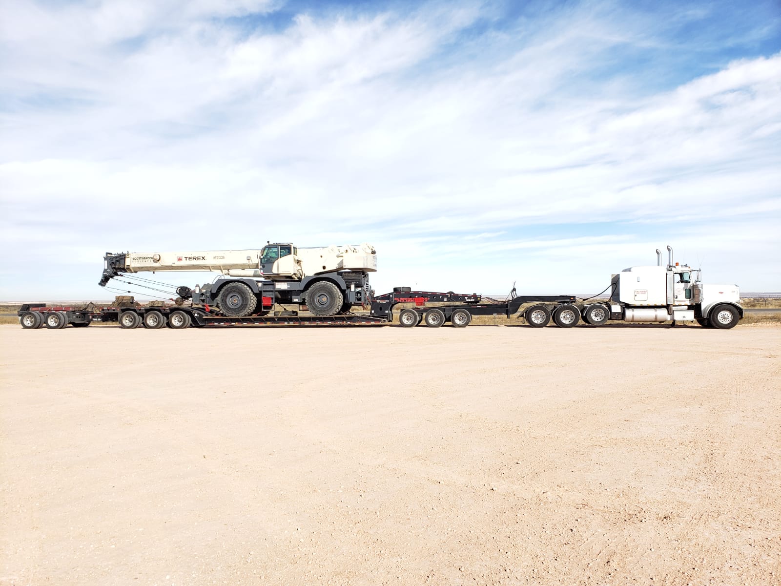 White Peterbilt hauling a Terex rough terrain crane on a multi-axle lowboy in West Texas