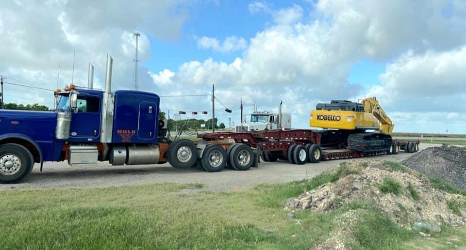 Blue Peterbilt with a Kobelco excavator loaded on a lowboy trailer