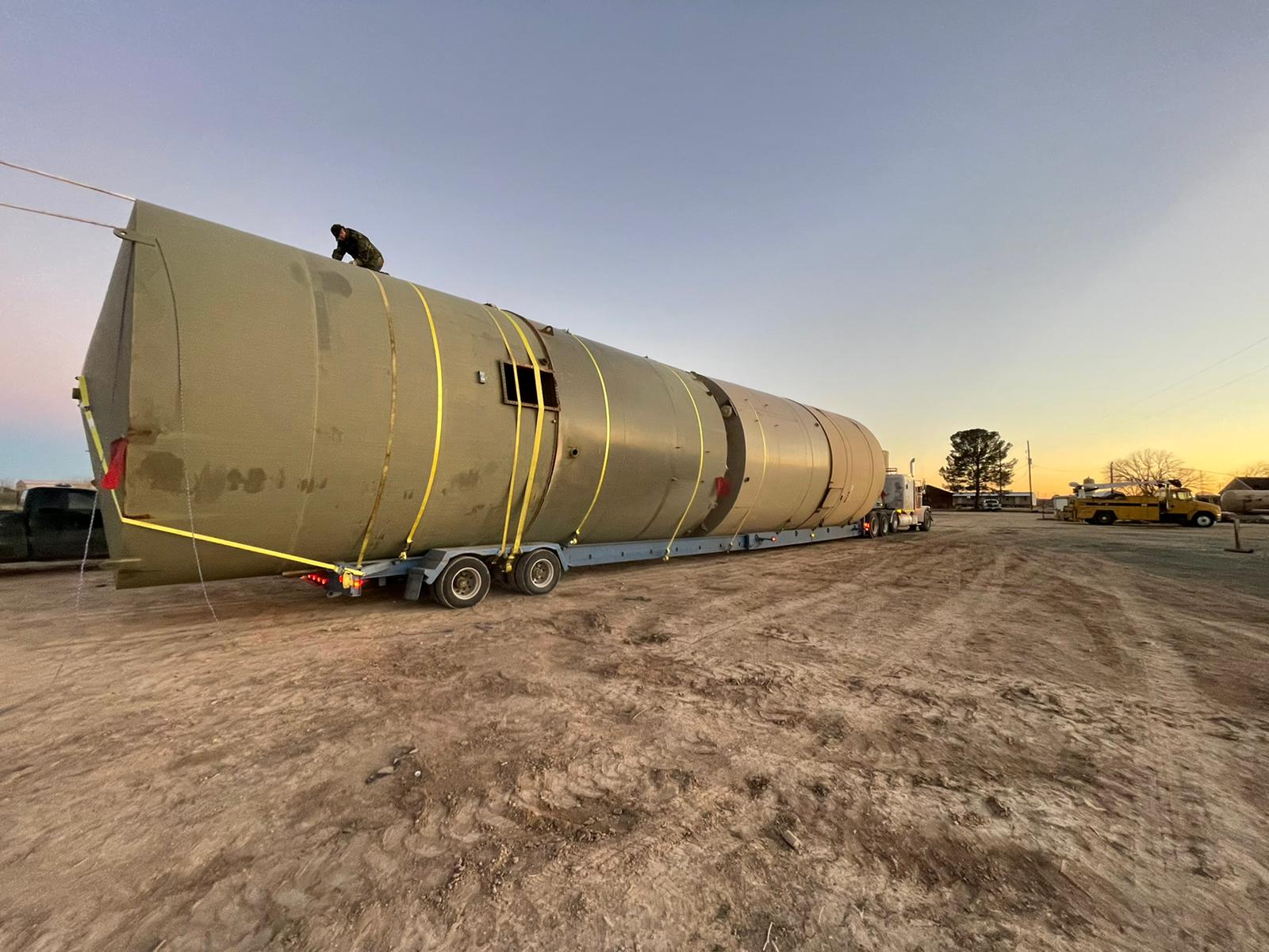 Peterbilt with a multi-axle trailer hauling an oversized steel silo vessel at sunset