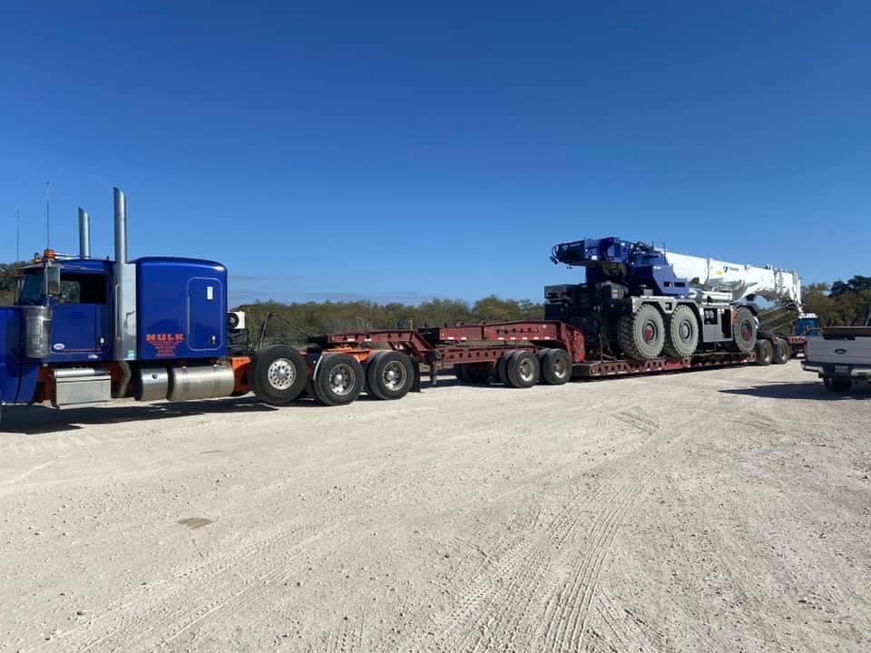 Blue Peterbilt hauling a white Tadano rough terrain crane on a multi-axle trailer
