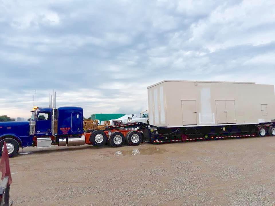 Blue Peterbilt hauling a large modular building on a perimeter frame trailer