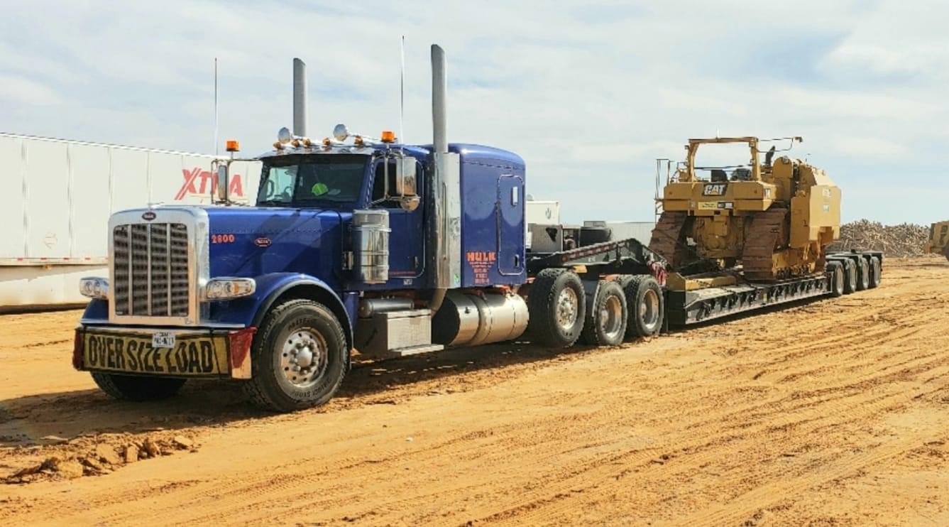 Blue Peterbilt with oversize load banner hauling a Caterpillar dozer in the oilfield
