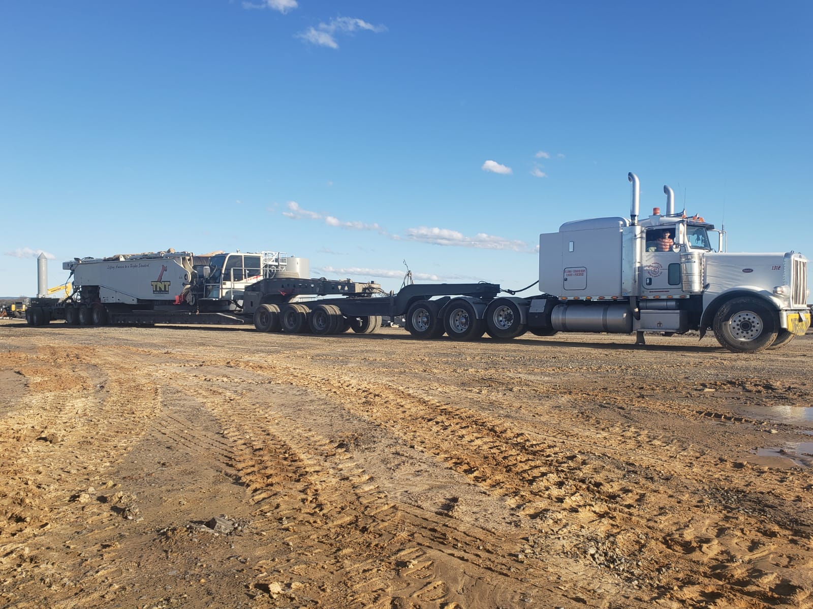 White Peterbilt hauling TNT crane counterweights and components on a double drop trailer